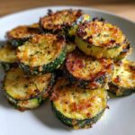 Close-up of golden brown, cheesy baked parmesan zucchini slices piled on a white plate.