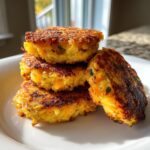 A stack of four golden brown, crispy mashed potato cakes seasoned with herbs, sitting on a white plate.