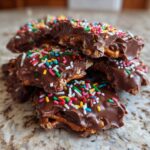 Close-up of broken pieces of crockpot Christmas crack topped with chocolate and festive rainbow sprinkles.