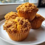 Four freshly baked sweet potato muffins with a thick, brown sugar crumb topping on a white plate.