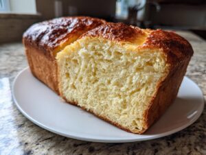A freshly baked loaf of rich, golden-brown brioche bread, sliced open to show the soft, yellow crumb.