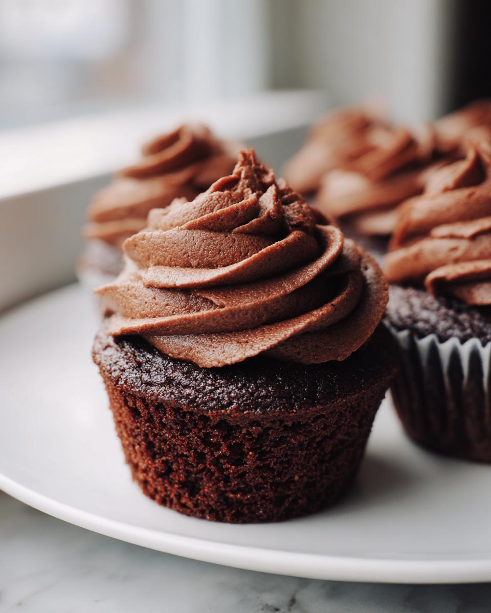 Close-up of one of the easy chocolate cupcakes featuring a dark, moist cake base and a tall swirl of chocolate buttercream frosting.