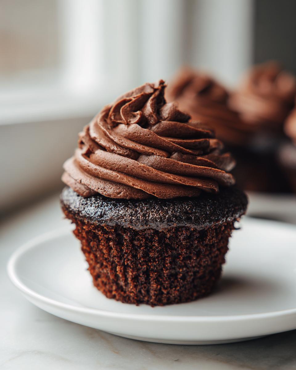 A close-up of one perfect, moist easy chocolate cupcakes topped with swirled chocolate buttercream frosting on a white plate.