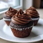 Close-up of one of the easy chocolate cupcakes topped with rich, swirled chocolate frosting on a white plate.