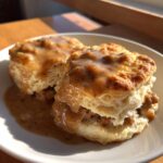 Two fluffy biscuits smothered in rich sausage gravy, served on a white plate, highlighting the texture of the biscuits and gravy.