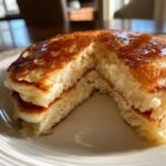 Close-up of fluffy buttermilk pancakes cut open to show the airy interior, drizzled with syrup.