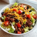A close-up view of a delicious taco salad featuring seasoned ground beef, shredded cheese, tomatoes, and black olives over lettuce.