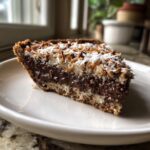 A close-up slice of rich German chocolate pie featuring layers of dark chocolate filling and toasted coconut topping.