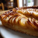 A close-up, appetizing shot of a slice of glazed apple tart showing thinly sliced, caramelized apples.