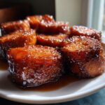 Several thick slices of glossy, caramelized candied sweet potatoes sitting in a pool of syrup on a white plate.