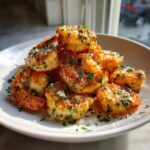 A pile of golden, crispy air fryer shrimp seasoned with chopped parsley and grated Parmesan cheese.