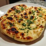 Close-up of two pieces of golden brown homemade naan bread topped with melted butter and fresh parsley.