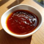 Close-up of thick, glossy, dark brown homemade teriyaki sauce in a small white dipping bowl.