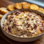 Close-up of a hot, bubbly reuben dip topped with melted cheese, served with toasted bread for dipping.