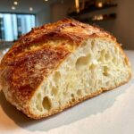 Close-up of a freshly baked Italian bread loaf cut in half, showing an open, airy crumb and a deeply browned, crackly crust.