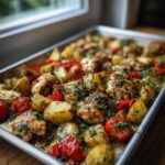 Close-up of juicy greek chicken thighs roasted on a sheet pan with potatoes and cherry tomatoes.