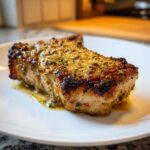 A thick, juicy pork chop seared to perfection with a golden, herbed crust, resting in its pan juices.