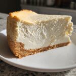 A thick, creamy slice of Keto cheesecake with a golden brown crust, served on a white plate.