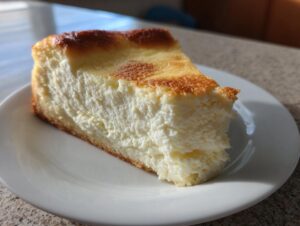 A thick, creamy slice of baked Keto cheesecake with a golden-brown top, served on a white plate.