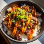 Close-up of Korean BBQ steak rice bowls topped with spicy orange sauce and green onions.