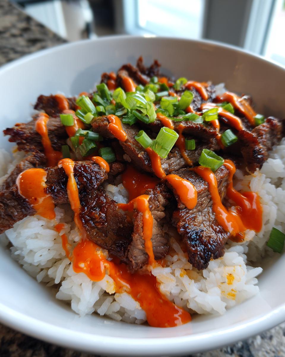 A close-up of Korean BBQ steak rice bowls featuring marinated steak over white rice, drizzled with bright orange sauce and green onions.