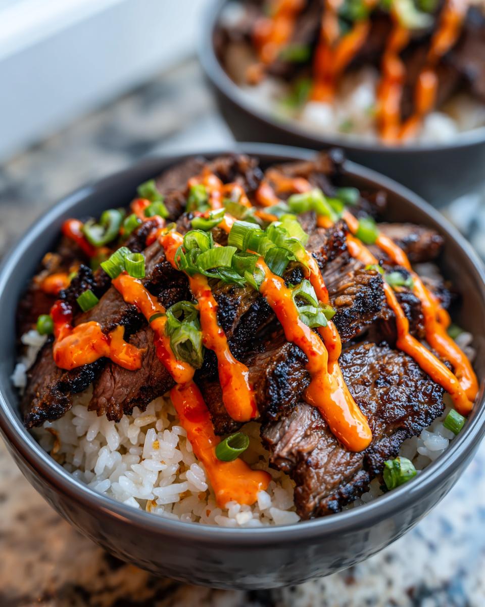 Close-up of a Korean BBQ steak rice bowl topped with grilled marinated steak, spicy orange sauce, and sliced green onions.