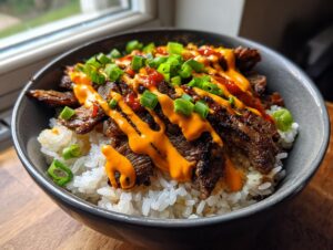 Close-up of a bowl filled with white rice, topped with sliced Korean BBQ steak, drizzled with orange sauce and green onions.