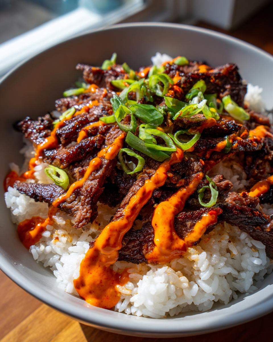 Close-up of Korean BBQ steak rice bowls featuring caramelized steak strips over white rice, drizzled with spicy orange sauce and green onions.