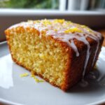 Close-up of a moist slice of lemon olive oil cake topped with white glaze and zest.