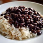 A close-up shot of a white bowl filled with fluffy white rice topped generously with seasoned black beans and rice.