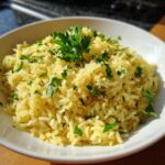 A white bowl filled with bright yellow mediterranean rice, topped generously with chopped fresh parsley.
