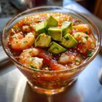 Close-up of a glass filled with vibrant mexican shrimp cocktail, topped with diced avocado.