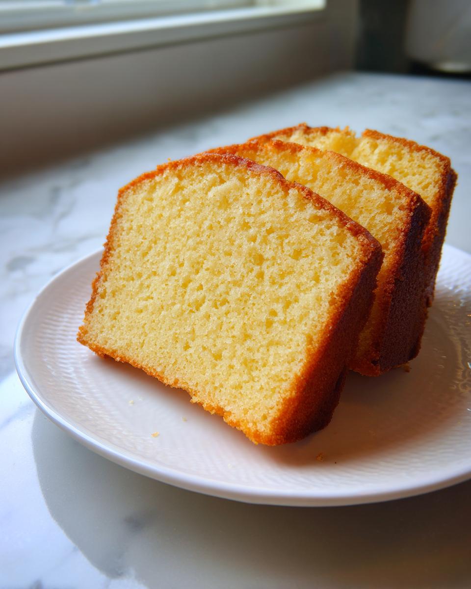 Three thick, moist slices of golden yellow million dollar pound cake served on a white plate.