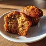 Close-up of a honey bran muffin cut in half showing the moist, textured interior next to a whole muffin.