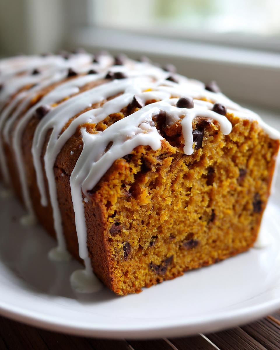 Close-up of a slice of moist pumpkin bread topped with white glaze drizzle and chocolate chips.