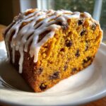 Close-up of a moist slice of pumpkin bread filled with chocolate chips and topped with a white vanilla glaze.