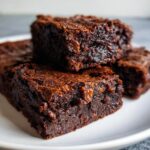 Close-up of rich, fudgy sweet potato brownies stacked on a white plate, showing moist texture.