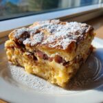 A thick slice of Monte Cristo breakfast casserole, dusted heavily with powdered sugar, served on a white plate.
