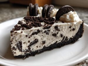A close-up of a rich slice of oreo cheesecake with a dark crust, creamy filling, and Oreo cookie garnish.