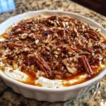 A rich pecan pie dip in a white dish, featuring a creamy base topped with candied pecans and caramel drizzle.