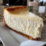 A perfect, tall slice of creamy cheesecake with a thick graham cracker crust, showcasing a smooth texture.