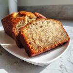 Close-up of two slices of moist Protein banana bread, showing the speckled interior texture, served on a white dish.
