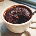 Close-up of a rich, dark chocolate mug cake topped with chocolate chips, with a spoon inserted.