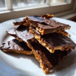 A stack of broken pieces of rich saltine cracker toffee with a thick chocolate topping on a white plate.