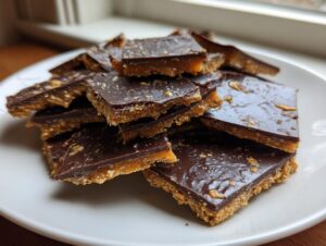 A stack of homemade saltine cracker toffee squares with a thick chocolate topping on a white plate.