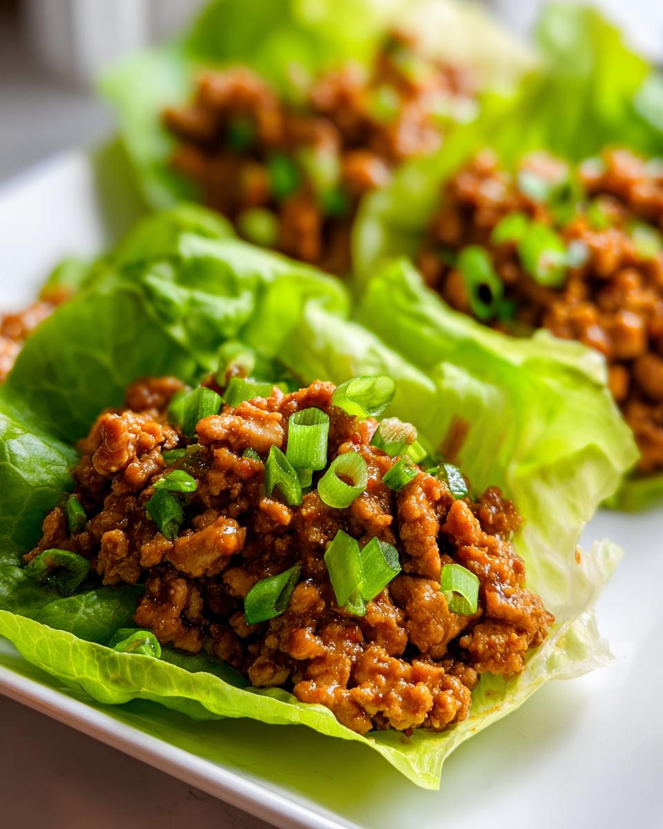 Close-up of savory seasoned ground chicken filling served in crisp lettuce cups, topped with fresh green onions, making perfect chicken lettuce wraps.