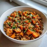 A close-up of a white bowl filled with a savory sweet potato skillet mixture, featuring diced orange sweet potatoes and ground meat, topped with fresh parsley.