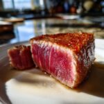 Close-up of a perfectly seared, rare tuna steak showing a bright red center, seasoned with spices, following a MARINADE FOR TUNA STEAK.