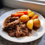 A plate featuring shredded beef from slow cooker pot roast served with seasoned potatoes and carrots.