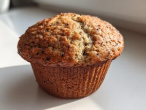 A single, golden-brown banana nut muffin with a domed, slightly cracked top, sitting on a white surface.